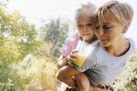 Mother carrying daughter piggyback in garden drinking a smoothie model released Symbolfoto property released  KNSF05097