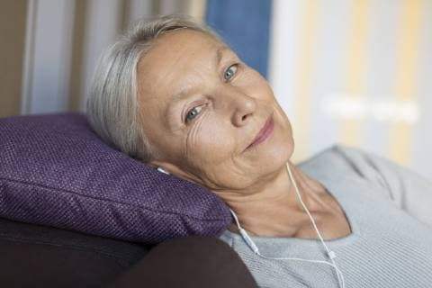 Portrait of smiling senior woman lying on the couch at home listening music with earphones model released Symbolfoto property released  VGF00121