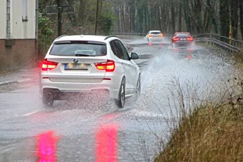 Gefährliche Straßenverhältnisse bei Starkregen. Das Wasser von einer nach Starkregen überfluteten Straße wird von den Autos in die Luft gerissen und sorgt bei vielen Fahrern für Schrecksekunden. Essen Nordrhein-Westfalen Germany - Deutschland Überruhr