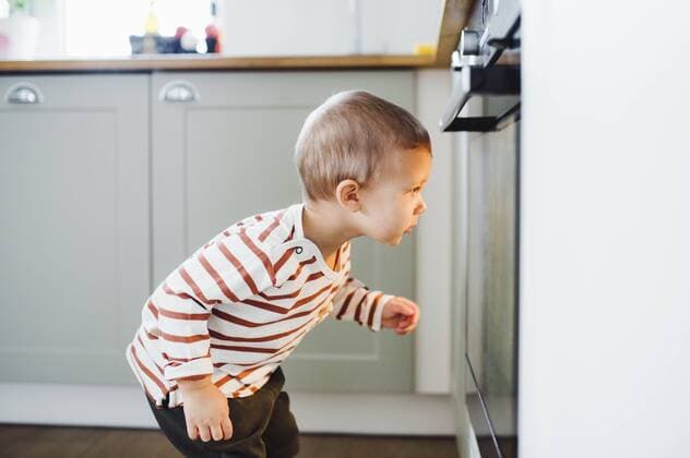 Toddler boy looking at oven in kitchen at home model released Symbolfoto property released  HAPF02833