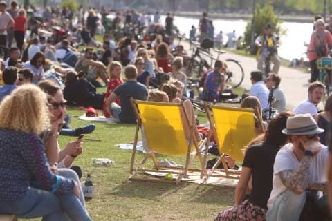 Frühlingstag am Ostermontag in Frankfurt: Sonnenhungrige genießen die warmen Temperaturen und die Sonnenstrahlen bei blauem Himmel auf einer Liegewiese am Mainufer in der Innenstadt, Hessen, Deutschland