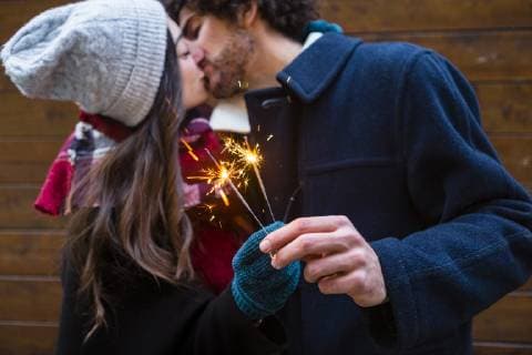 Young couple in winterwear kissing and holding sparklers in front of wooden wall model released Symbolfoto  MGIF00319