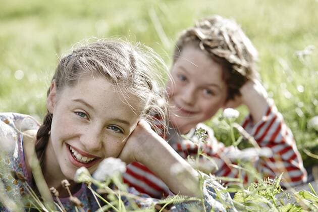Portrait of smiling girl lying on a meadow with little brother at the background model released Symbolfoto  RORF01743