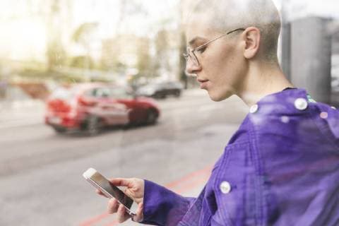 Young woman looking at her phone at the bus stop in the city model released Symbolfoto  WPEF01380