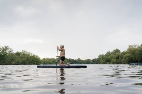 Senior man kneeling on SUP board model released Symbolfoto  GUSF01797