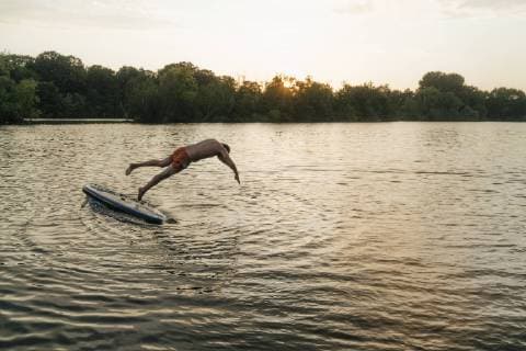 Man jumping from SUP board on a lake at sunset model released Symbolfoto  GUSF01827