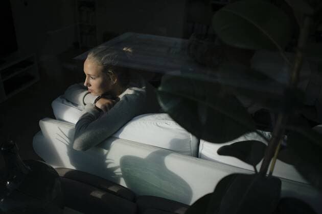 Serious teenage girl sitting on couch at home looking out of window model released Symbolfoto property released  JOSF02940