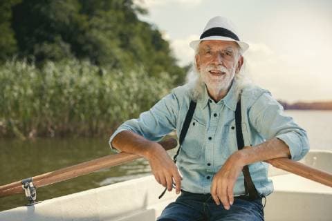 Portrait of senior man sitting in rowing boat on a lake wearing suspenders and summer hat model released Symbolfoto  VWF00018