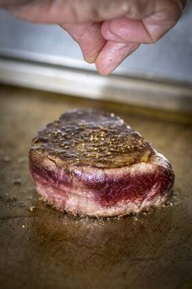 Female cook flavouring beef fillet with pepper model released Symbolfoto  HAMF00570
