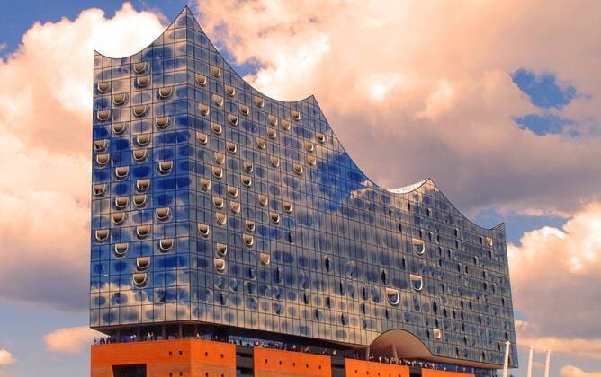 Wolken und blauer Himmel spiegeln sich in der Fassade der Elbphilharmonie im Hamburger Hafen. (Bearbeitet).