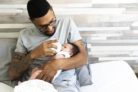 Father bottle-feeding his newborn baby in bed model released Symbolfoto property released ERRF01311