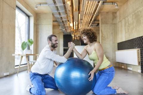 Happy man and woman arm wrestling on fitness ball in modern office model released Symbolfoto property released  FMKF05656