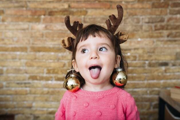 Portrait of toddler girl sticking out tongue wearing reindeer antlers headband and Christmas baubles model released Symbolfoto  GEMF02944