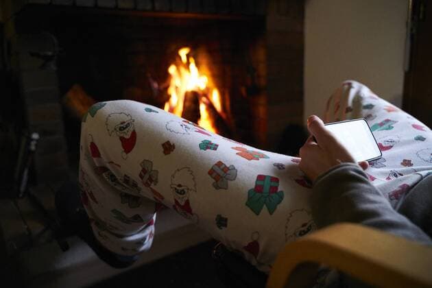 Man sitting in front of fireplace wearing Santa Claus Christmas pants using mobile phone model released Symbolfoto  GEMF02961