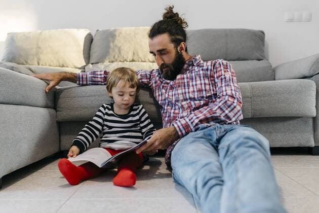 Father and little daughter sitting in the floor in the living room reading a book together model released Symbolfoto property released  JRFF02988