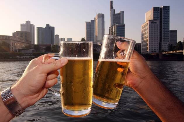 Einen warmen Sommerabend genießen zwei Männer am Mainufer vor dem Bankenviertel und stoßen mit einem Bier an, Frankfurt, Hessen, Deutschland