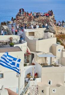Tourists on Oia Castle wait for the sunset with Caldera View and the famous Windmill in Oia, Santorini , Greece at 04 June 2019. Photographer: Peter Schatz