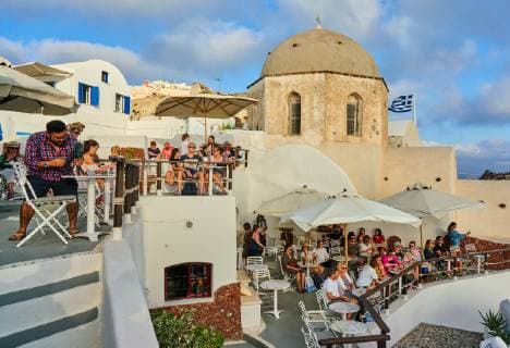 Tourists in restaurants and on Oia Castle wait for the sunset with Caldera View and the famous Windmill in Oia, Santorini , Greece at 04 June 2019. Photographer: Peter Schatz