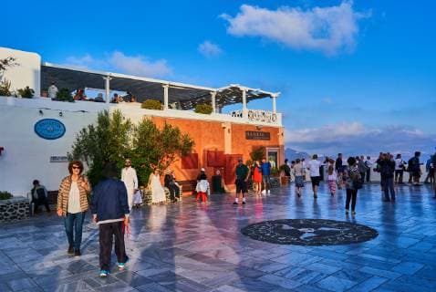 Tourists in restaurants and on Oia Castle wait for the sunset with Caldera View and the famous Windmill in Oia, Santorini , Greece at 04 June 2019. Photographer: Peter Schatz
