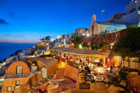 Tourists in luxury restaurants and on Oia Castle wait for the sunset with Caldera View and the famous Windmill in Oia, Santorini , Greece at 04 June 2019. Photographer: Peter Schatz