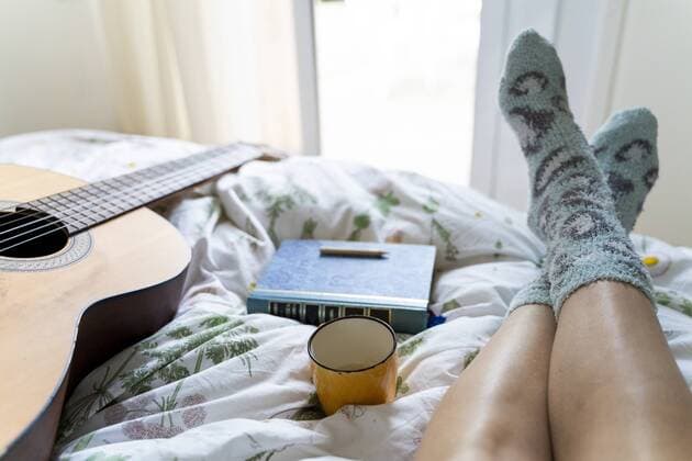 Woman lying on bed with guitar, book and cup of coffee, partial view model released Symbolfoto  AFVF03474