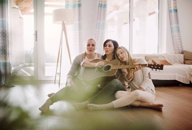 IMAGO Creative: Bildung, Musikerziehung Tag der Musik am 21. Juni Mature woman with two daughters sitting on the floor playing guitar at home model released Symbolfoto property released  HAPF02965