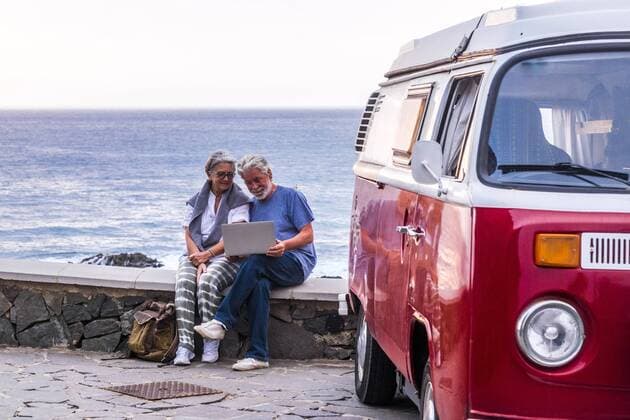 Senior couple traveling in a vintage van, using laptop, sitting on a wall at the sea model released Symbolfoto  SIPF02019