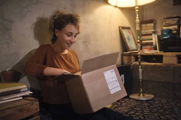 Amazed young woman unpacking parcel at home model released Symbolfoto property released  GCF00314