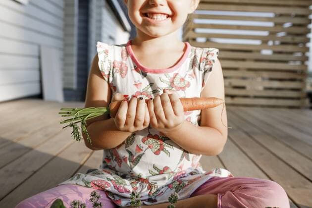 Creative Highlights Symbolfoto Little girl sitting on terrace holding carrot, partial view model released Symbolfoto property released  KMKF01022