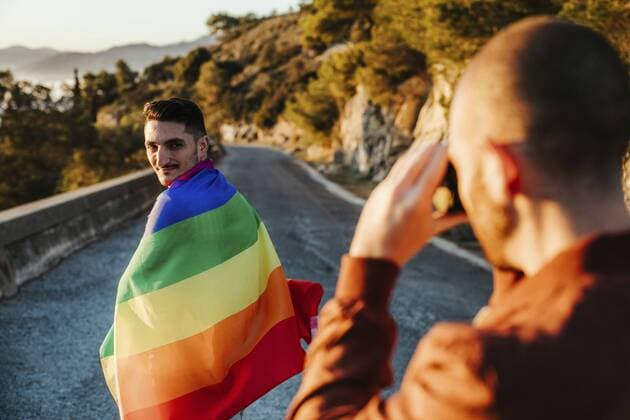 Photographer taking picture of man wrapped in a gay pride flag on a road in the mountains model released Symbolfoto  LJF00507