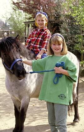  Outdoor, blondes Maedchen fuehrt ein Pony am Halfter, auf dem ein Junge reitet,model released, Symbolfoto  Copyright: xnsp226bMicrox Panthermedia23617126