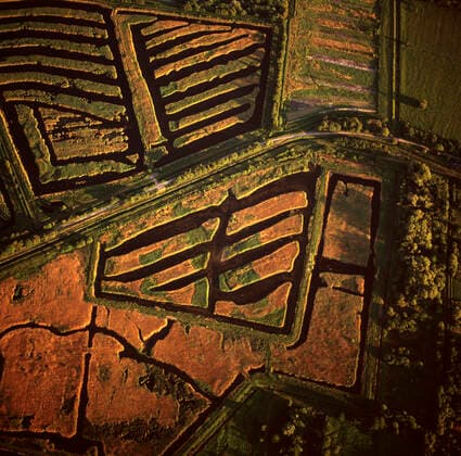 IMAGO Nature: Unsere Erde, Ressourcen, Torf England - Aerial view, Peat Extraction, Westhay Moor. near Glastonbury, Somerset. At the beginning of the 20th century mechanised diggers were used to create machine cut trenches. The peat was then stacked in blocks to dry. It still happens today, but is strictly limited. The geometrical patterns formed by the dark peat and gleaming water, remain a characteristic symbol of the Levels around the River Brue.  Copyright: DaexSasitorn 10741287