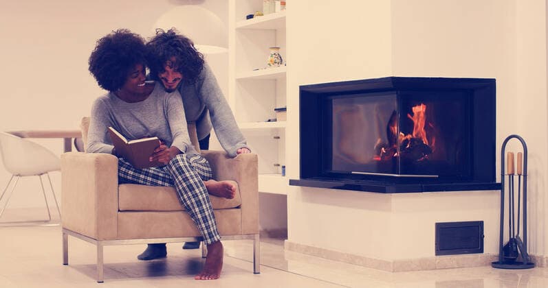 Young beautiful multiethnic couple hugging in front of fireplace at home when reading a book at autumn day,model released, Symbolfoto ING_32193_160000