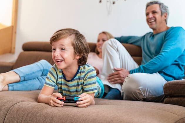 Boy lying on couch at home playing video game with parents watching model released Symbolfoto property released  DIGF08195