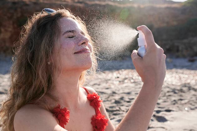 IMAGO Creative, Jahreszeit Sommer, Sonnenschutz Young woman applying suncream spray on the beach model released Symbolfoto  IGGF01320