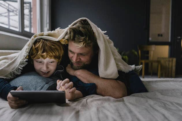 Father and son lying together under blanket looking at digital tablet model released Symbolfoto property released  KNSF06291