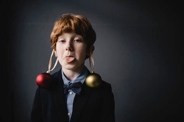 Portrait of redheaded boy wearing bow tie and Christmas baubles sticking out tongue model released Symbolfoto property released  KNSF06304