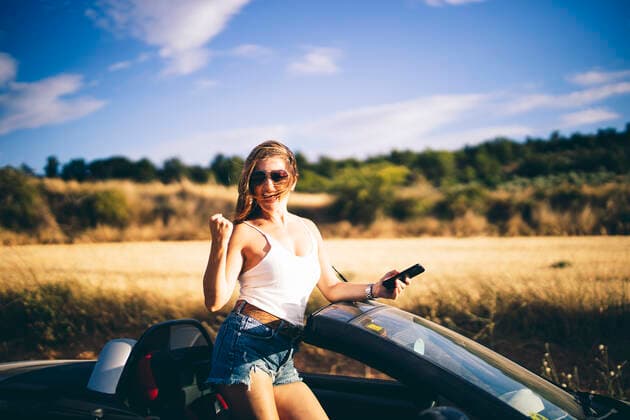 Woman standing in her convertible, holding smartphone, happy about good news model released Symbolfoto  OCMF00610