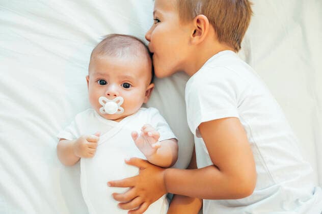 IMAGO Kreativ: Bruderschaft Older brother kissing baby boy in bed model released Symbolfoto  OCMF00632
