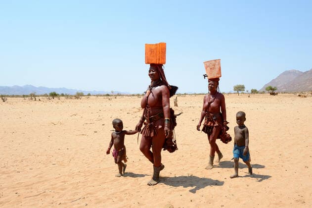 IMAGO Cultures of the world, Himba Volk in Namibia Himba women and children returning from the waterpoint, carrying plastic cans full of water, during dry season, Marienfluss Valley, Kaokoland Desert, Namibia. October 2015  1531100 EricxBaccega