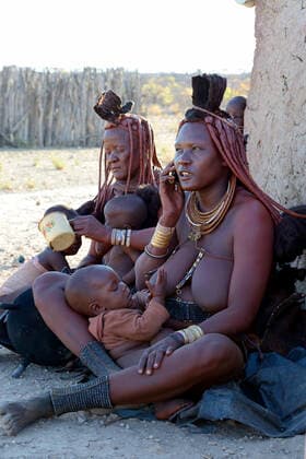IMAGO Cultures of the world, Himba Volk in Namibia Himba woman with traditional hair and jewellery, breastfeeding whilst on a mobile phone nursing her baby. Kaokoland, Namibia October 2015  1531162 EricxBaccega
