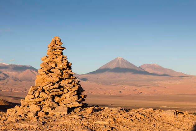 Apacheta Apachita - a stone cairn in the Andes, a little pile of rocks built along the trail in the high mountains with Licancabur volcano (5916 m above sea level) and Juriques volcano to the far right (5704 m) in the background, Atacama Desert, San Pedro, Chile  1561566 ChristophexCourteau