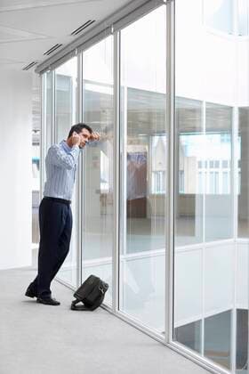 Office worker talking on mobile phone looking out window of empty office space,model released, Symbolfoto,property released 03B71945