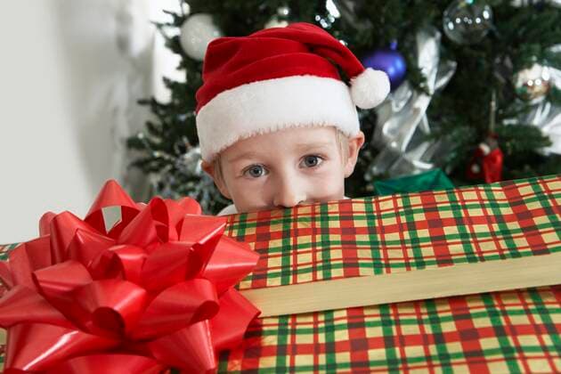 Boy (5-6) in Santa costume peeking over present by Christmas tree,model released, Symbolfoto,property released 03B99890