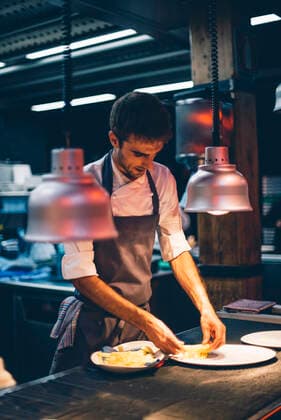 Chef serving food on plates in the kitchen of a restaurant model released Symbolfoto property released  CJMF00109