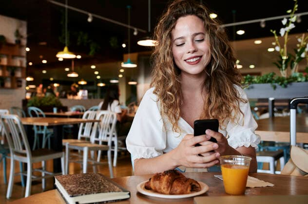 Smiling young woman using smartphone in a cafe while having breakfast model released Symbolfoto  IGGF01332