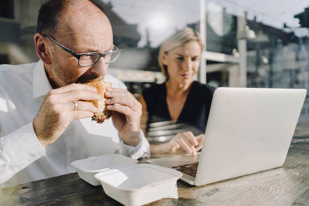 Businessman eating hamburger in coffee shop, while colleague is using laptop model released Symbolfoto property released  KNSF06379
