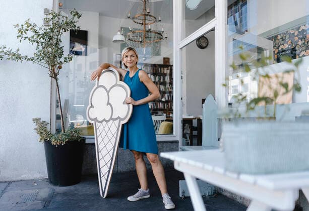 Woman standing in front of her coffee shop, holding icecream sign model released Symbolfoto property released  KNSF06399