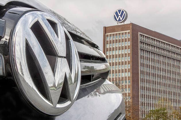 VW Abzeichen von einem Auto aus der VW Produktion mit dem VW Verwaltungsgebäude (mit neuem VW Emblem) in Wolfsburg - gesehen am 27.10.2019 auf dem Parkplatz an der Heinrich Nordhoff Str.