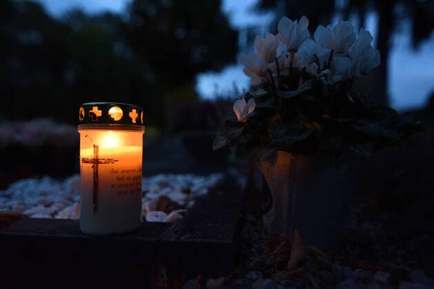 Grabkerze auf einem Grab eines kleinen Friedhofs. Auf dem Grablicht ist ein Kreuz und ein Spruch zu sehen. Rechts neben der Grableuchte steht eine Topfpflanze mit weißen Blüten. Grablicht auf einem Friedhof, Schwerte Nordrhein-Westfalen Deutschland *** Grave candle on a grave of a small cemetery A cross and a saying can be seen on the grave light To the right of the grave light stands a pot plant with white flowers Grave light on a cemetery, Schwerte Nordrhein Westfalen Germany